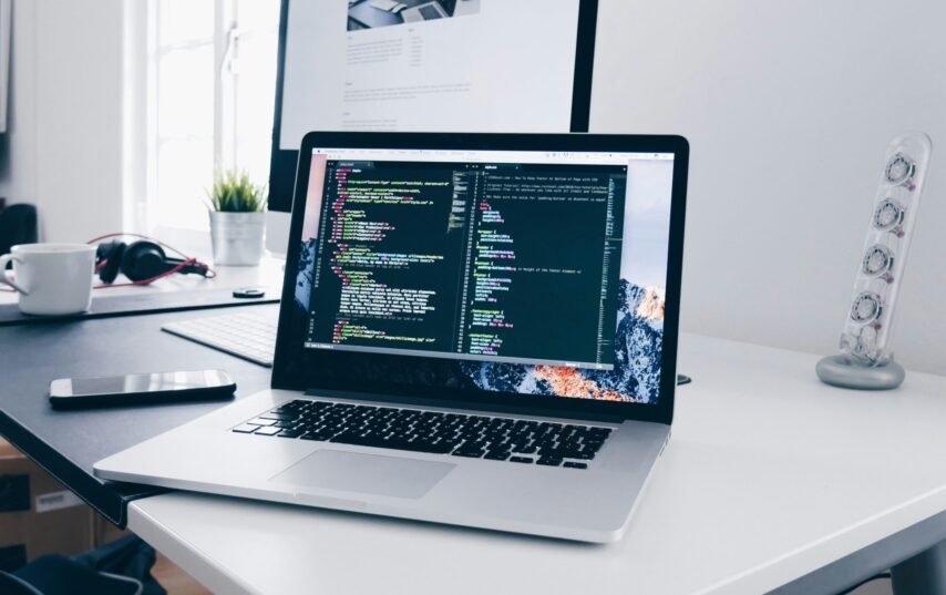 A MacBook with lines of code on its screen on a busy desk